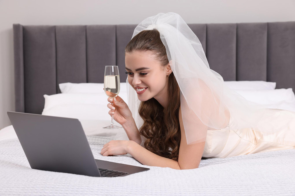 Bride laying on the bed in her bridal gown while looking at a computer screen