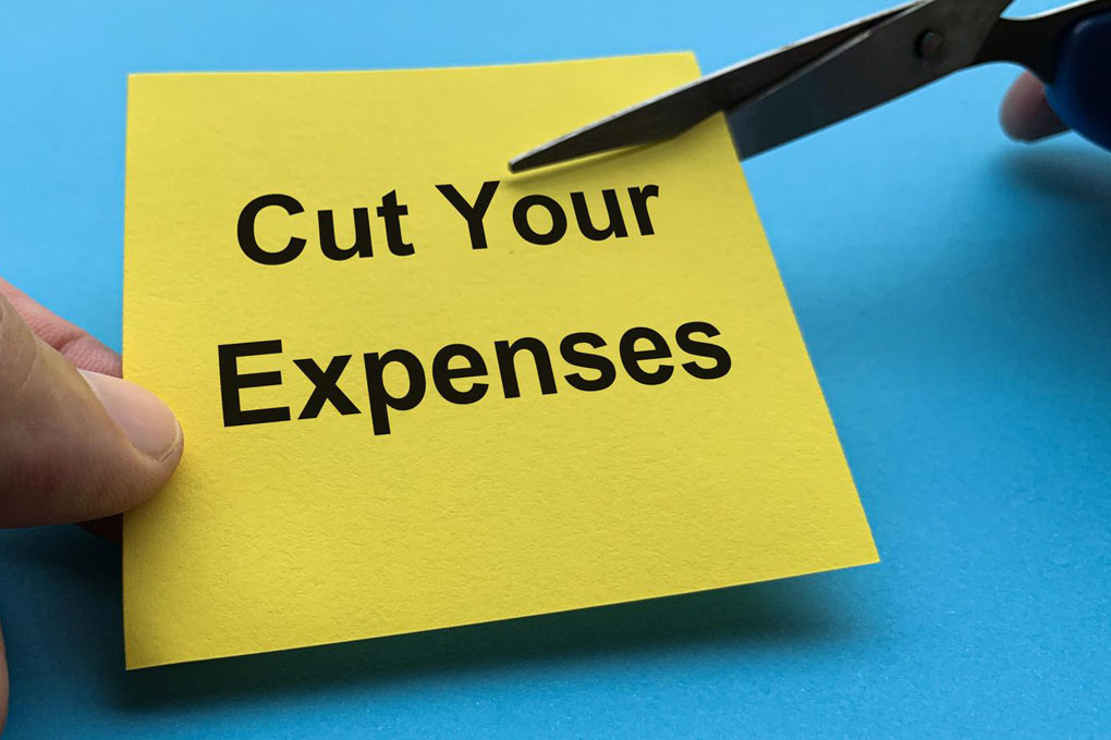 Sticky note with the word expenses is being cut with scissors