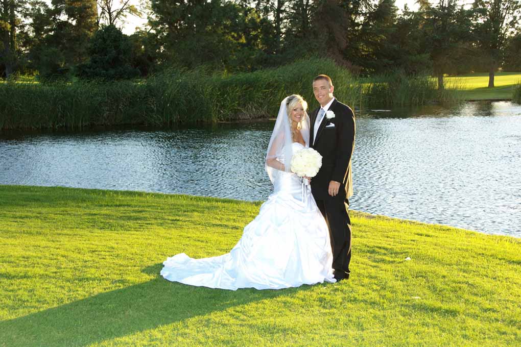 Bride dressed in her gown poses by lake with her groom
