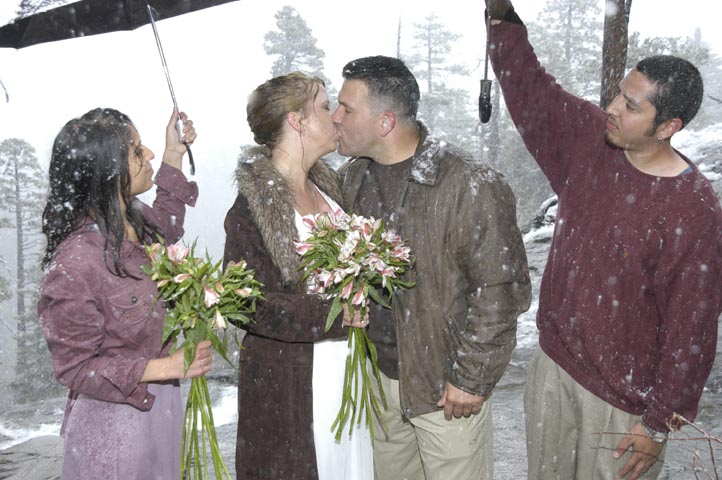 Two kissing in the snow under umbrellas.