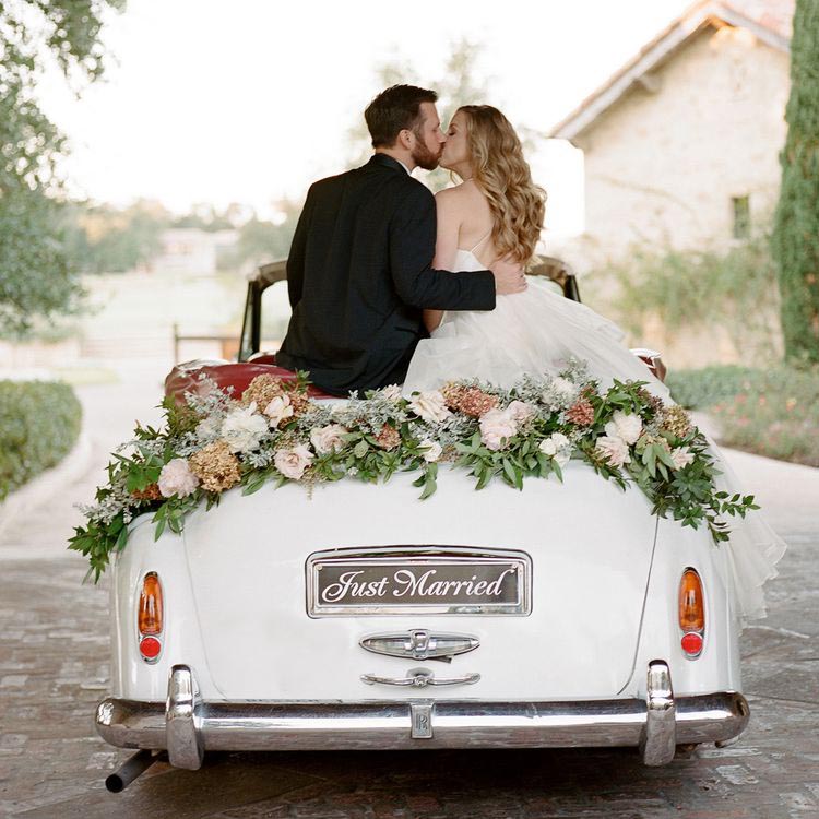 The newly married are driving away in a classic car