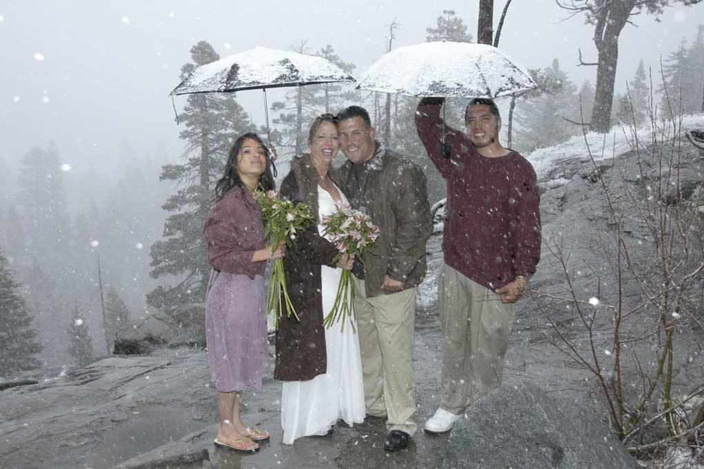 Bride under umbrella with groom as snow falls