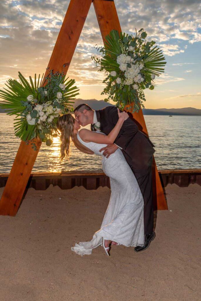 The bride leans back as the groom kisses her under the arbor