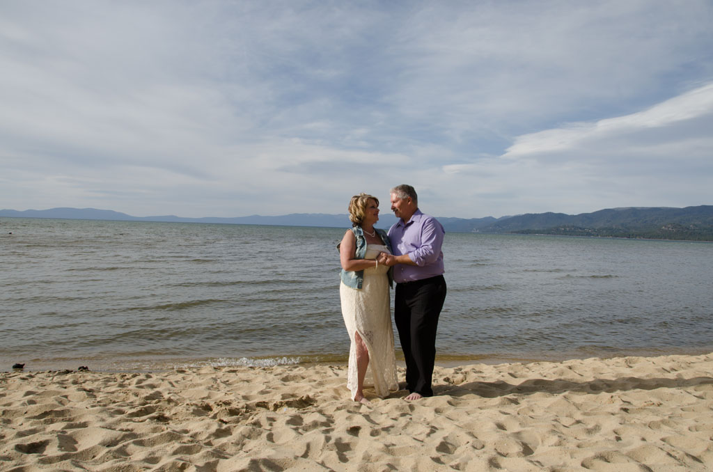 The bride and groom embraced together near the edge of the lake.