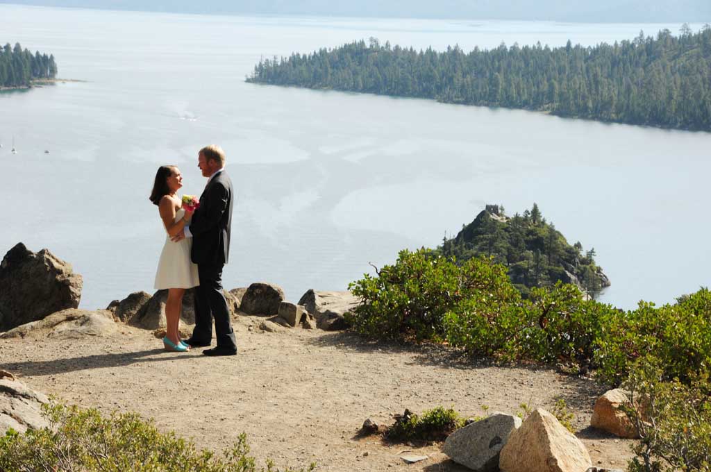 The newly married couple standing close to each other on the bluff of Emerald Bay