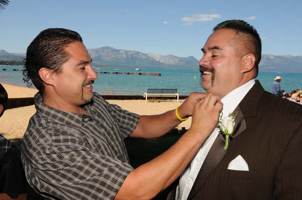 A friend pins the boutonniere onto the groom's tuxedo and adjusts his bow tie