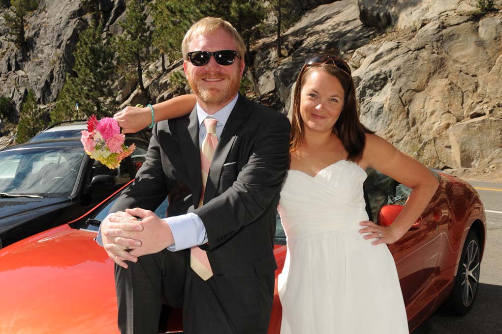 The bride and groom standing together next to their red car