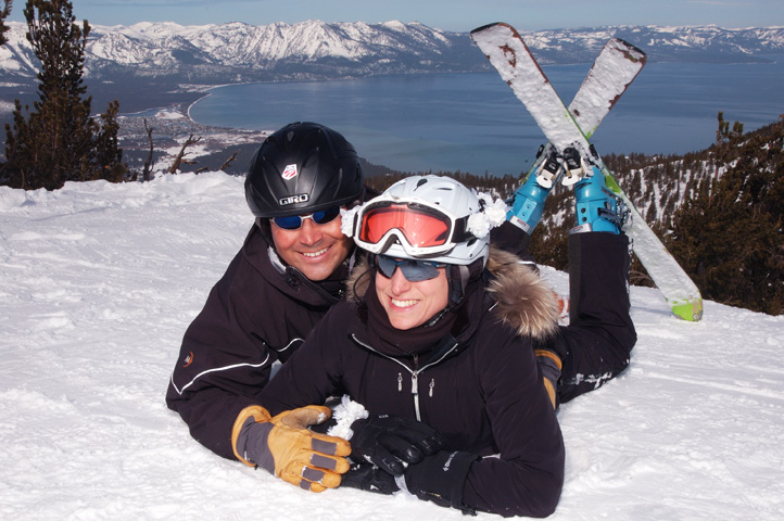 The newlyweds laying on the snow with their skis crossed